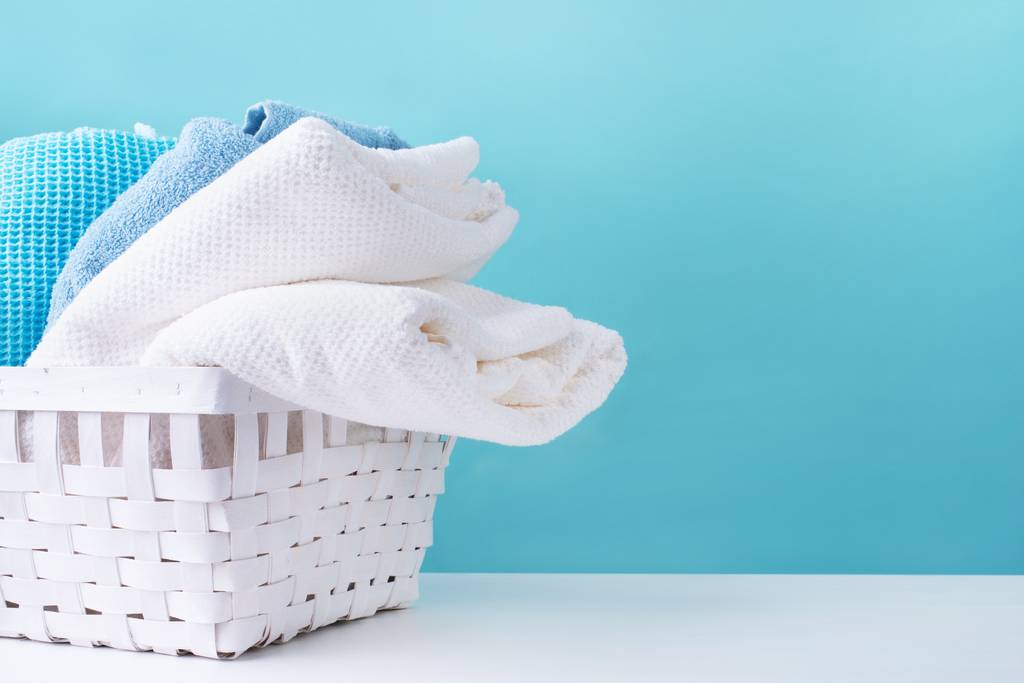 Pile de serviettes propres dans un panier à linge blanc isolé sur fond bleu.